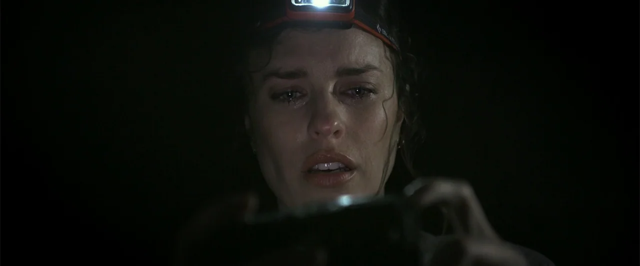 Black Water: Abyss (2020) movie still: closeup — A woman is surrounded by darkness with only artificial light sources visible. She holds a glowing…