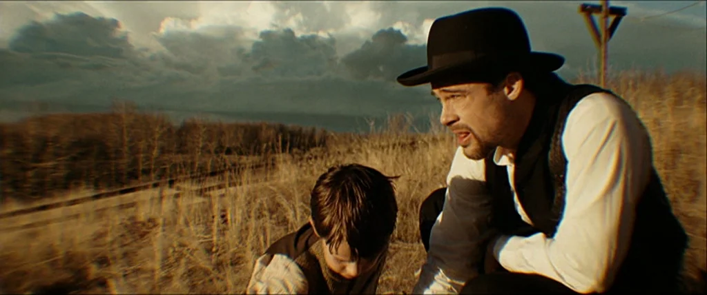 The Assassination Of Jesse James By The Coward Robert Ford (2007) movie still: medium — A man and child kneel in a desolate field of dry grass at…