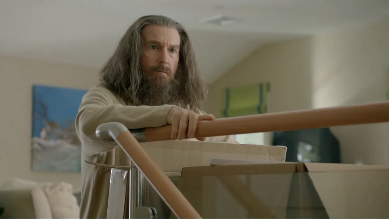 Clear History (2013) movie still: medium — A modern domestic staircase with a wooden handrail and glass panels overlooks a living area. A…