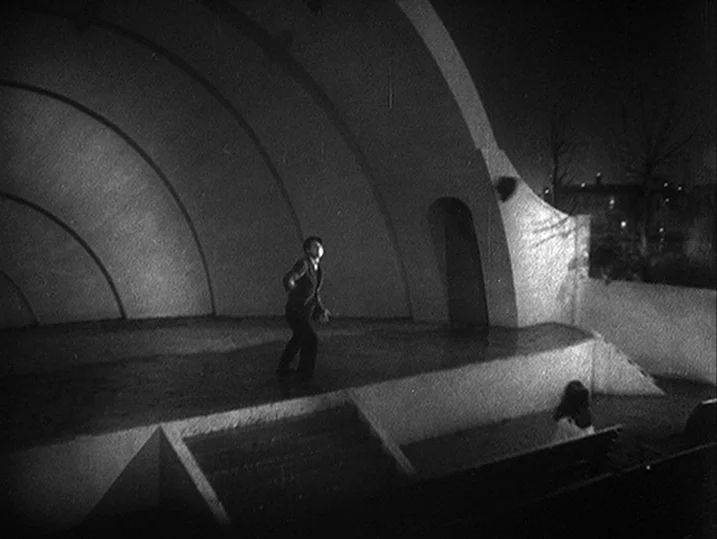 Anatomy of a Relationship (1976) movie still: wide — A concrete outdoor bandstand with a curved arched shell structure at night. A lone man stands…