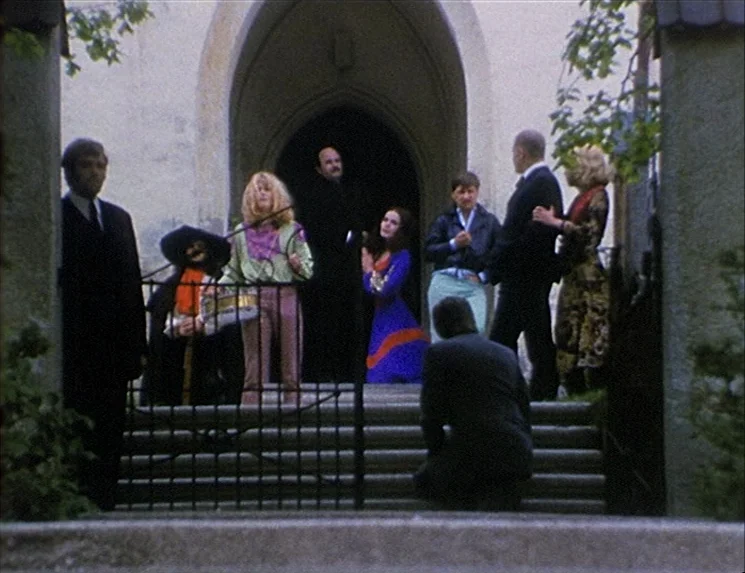The Niklashausen Journey (1970) movie still: wide — A group of people stands on stone steps leading to a dark arched doorway. A person in a suit…