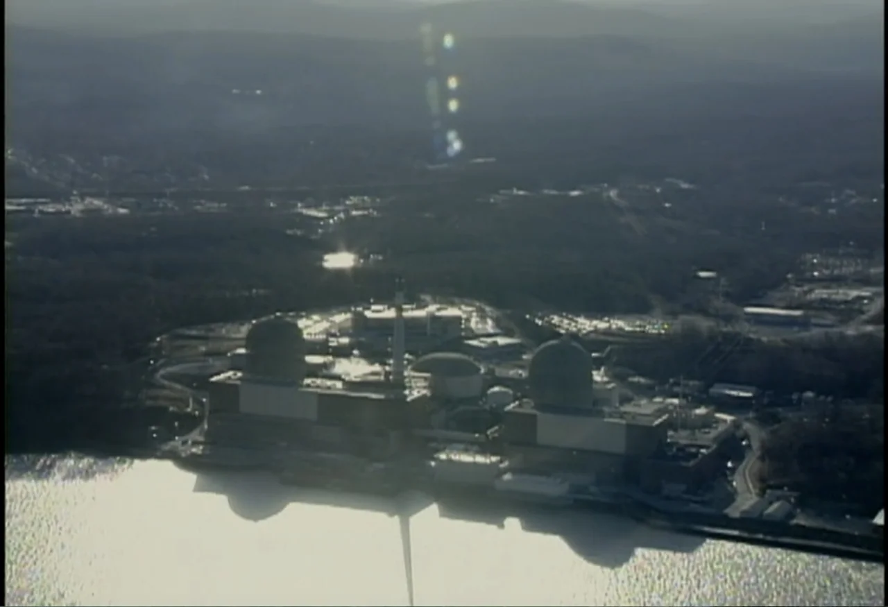 Indian Point: Imagining the Unimaginable (2004) movie still: establishing — A large nuclear power plant sits on a riverbank surrounded by dense…