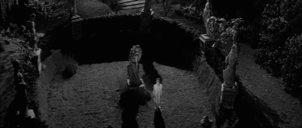 The Innocents (1961) movie still: wide — A dark circular sculpture garden features multiple stone statues arranged along a hedge boundary. A single…
