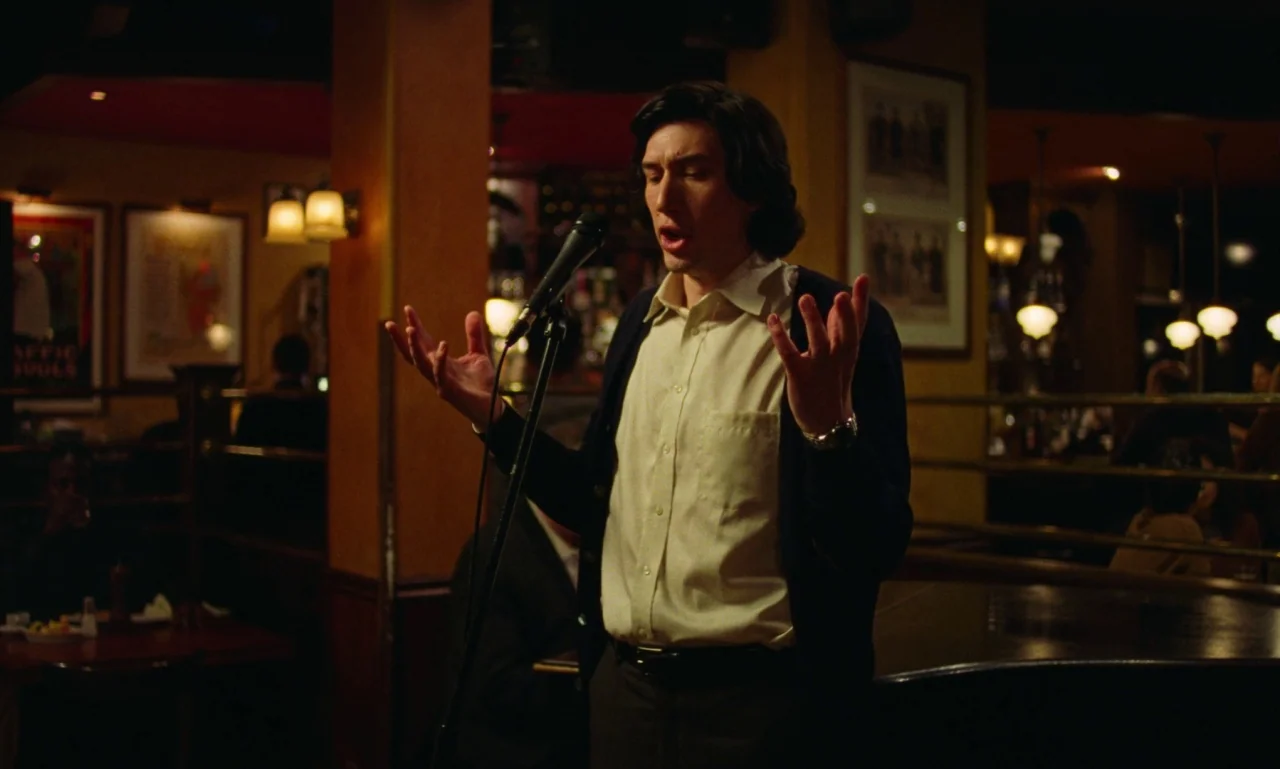 Marriage Story movie still: medium — A dimly lit bar setting with dark wooden interiors and soft warm overhead lighting. A man stands center frame…