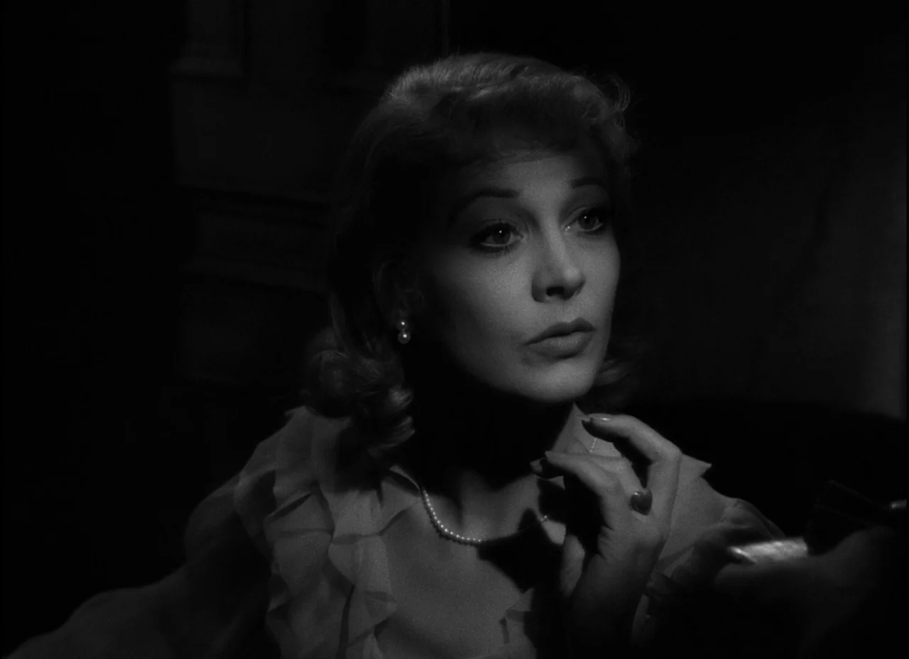 A Streetcar Named Desire (1951) movie still: closeup — A dark, minimally furnished room serves as the backdrop for a woman in formal wear. The woman…