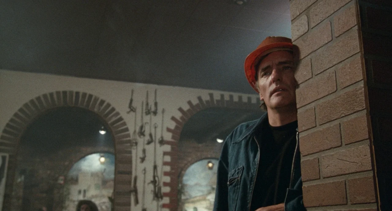 Out of the Blue (1980) movie still: medium — A dimly lit room features arched brick wall cutouts decorated with hanging metal tools. A middle-aged…