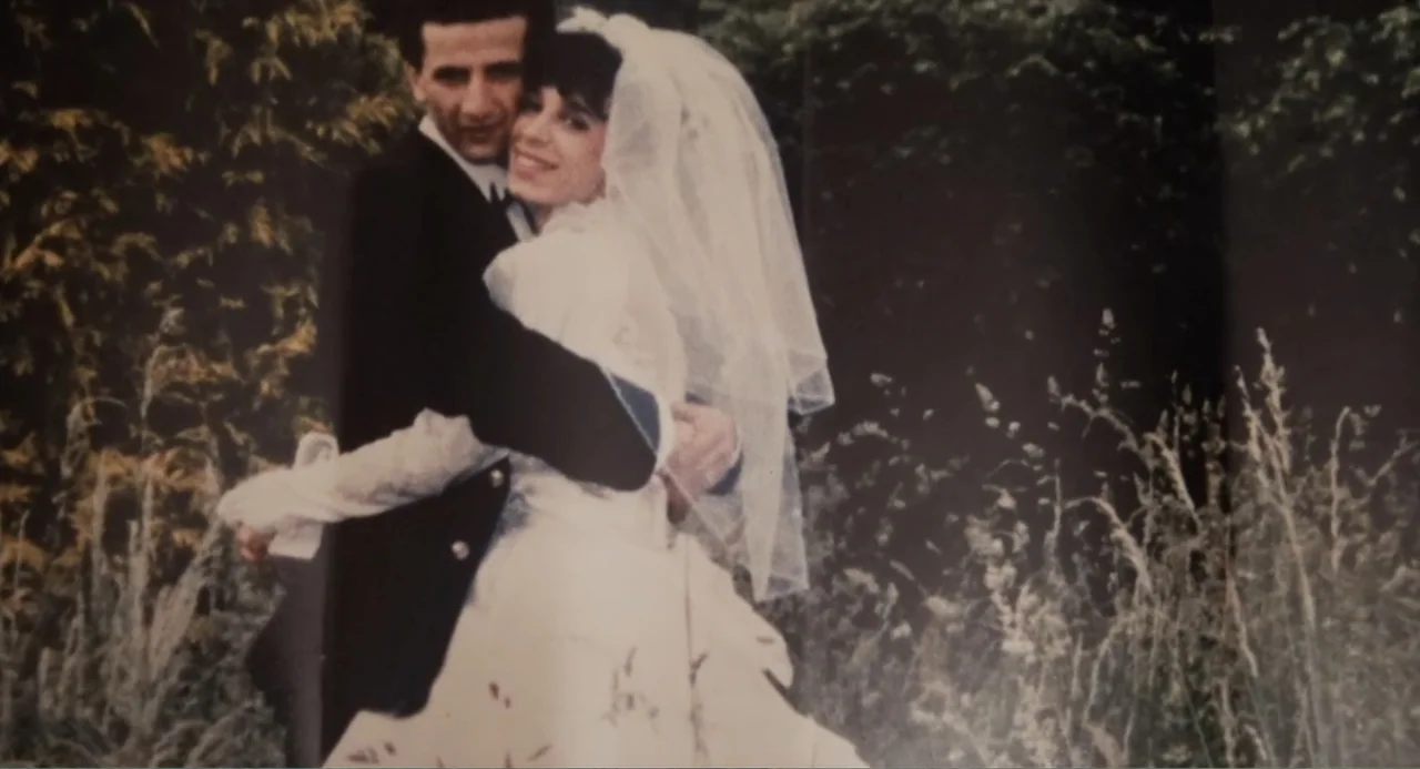 A Dramatic Film (2019) movie still: medium — A couple poses for a wedding portrait in a grassy outdoor field. The bride wears a traditional gown and…