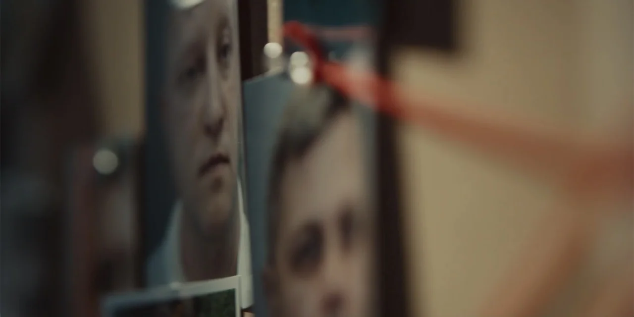 Navalny (2022) movie still: closeup — A wall surface with multiple portrait photographs clipped or pinned into place. The images are slightly…