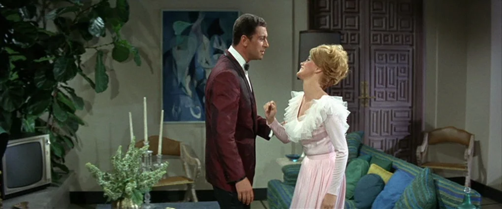 Viva Las Vegas (1964) movie still: medium — A 1960s interior space features mid-century furniture, a modern art piece, and potted plants. A man in a…