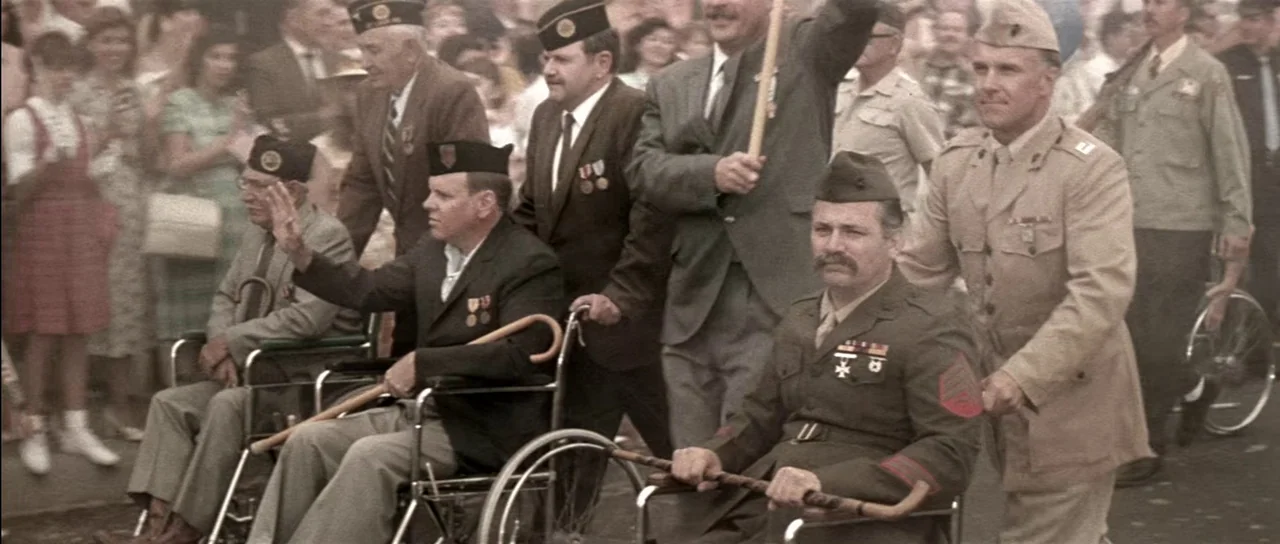 Born On The Fourth of July (1989) movie still: medium — A group of veterans in wheelchairs participates in a sunny outdoor parade procession. Men in…