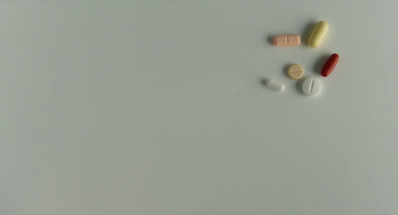 Pain and Glory (2019) movie still: wide — A selection of various pharmaceutical pills rests on a smooth, off-white tabletop surface. Seven different…