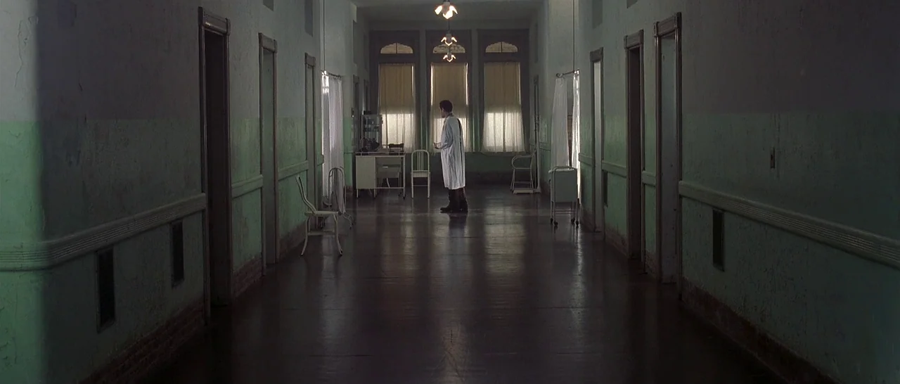 The Cider House Rules movie still: wide — A long, dimly lit hospital corridor features green-painted walls and a reflective wooden floor. A single…