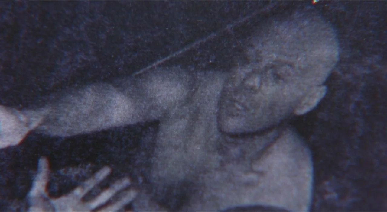 Twelve Monkeys (1995) movie still: closeup — A low-resolution, grainy image captured in an indeterminate dark space. A shirtless man with a shaved…