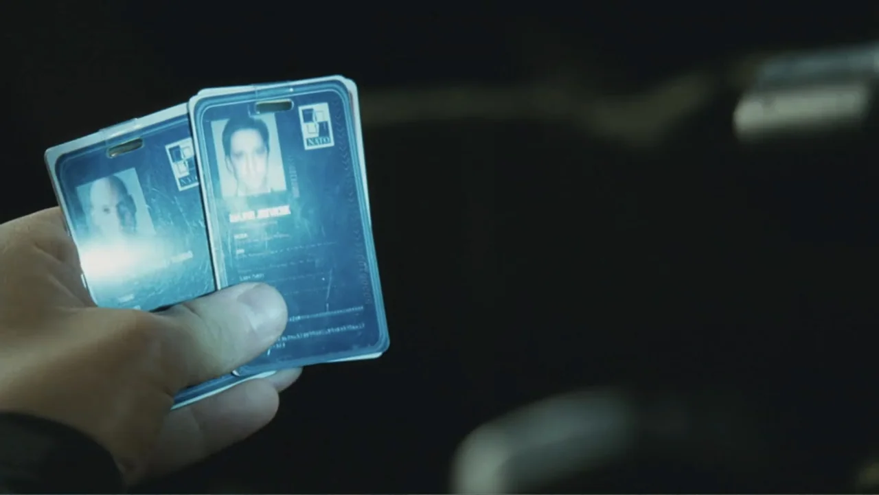 Salt (2010) movie still: closeup — A hand holds two plastic identification cards against a dark, featureless background. The cards feature printed…