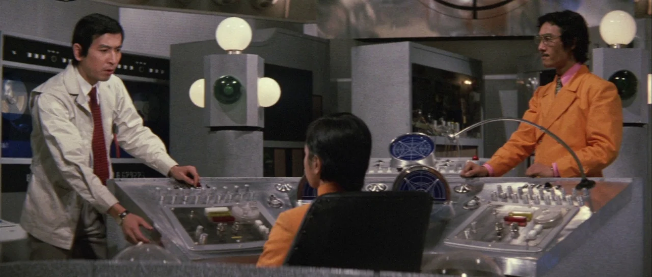 Godzilla Vs Gigan (1972) movie still: medium — A retro-futuristic laboratory features a large brushed-metal command console with numerous colored…