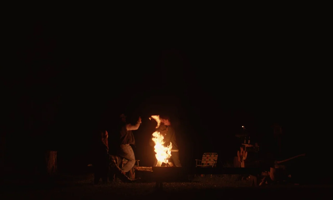 Mickey and the Bear (2019) movie still: wide — A dark outdoor space with a bright, crackling campfire as the central light source. Three individuals…