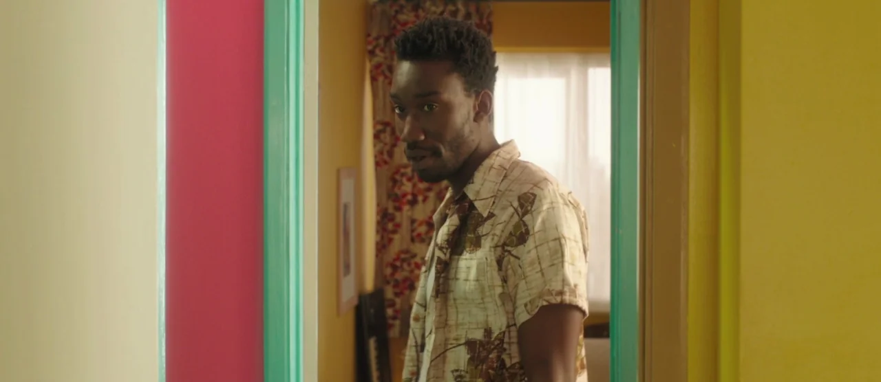 Dom Hemingway (2013) movie still: medium — A hallway with brightly colored walls including pink, turquoise, and yellow paint. A man stands in the…