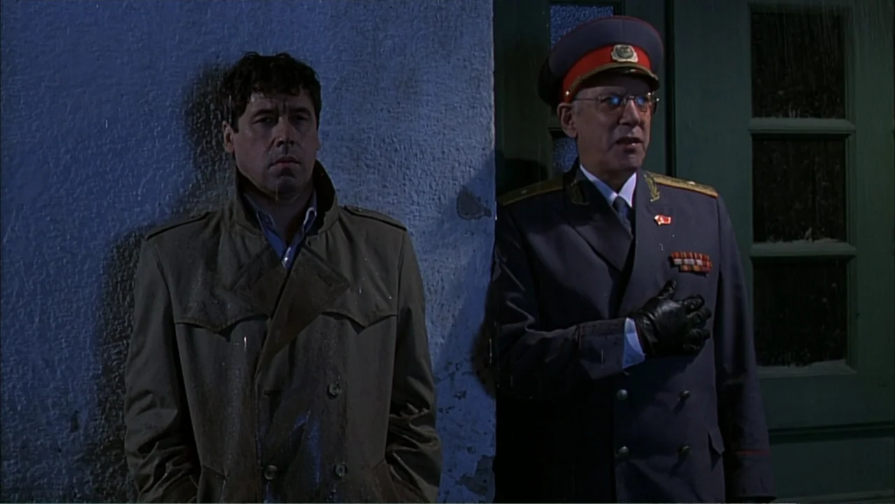Citizen X (1995) movie still: medium — A man in a trench coat and a man in a military uniform stand together. They lean against a textured white…