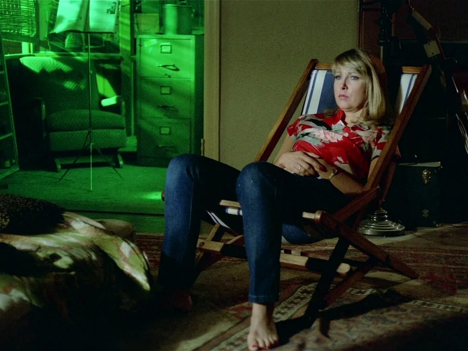 One From The Heart (1982) movie still: medium — A dark, cluttered interior space is dominated by a harsh, unnatural green light source. A blonde…