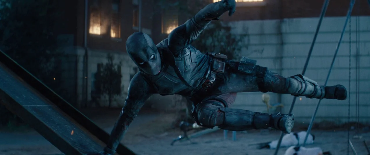 Deadpool 2 (2018) movie still: fullbody — A dark playground at night features swings and a metal slide in the background. A masked figure leaps…