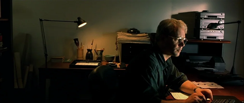The Insider (1999) movie still: medium — A dimly lit room containing a dark wood desk and electronic stereo equipment. A man sits at the computer,…
