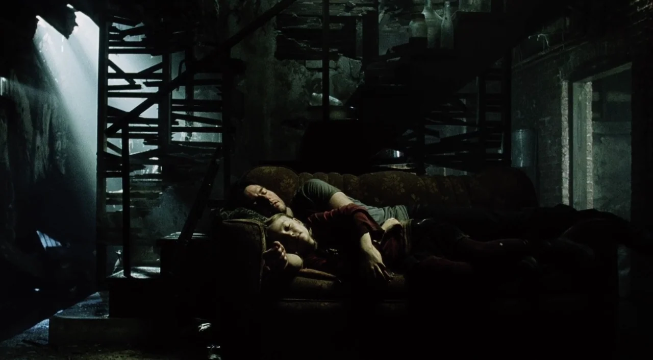 War of the Worlds (2005) movie still: medium — A dark, derelict interior space features a spiral metal staircase and exposed brick walls. Two people…