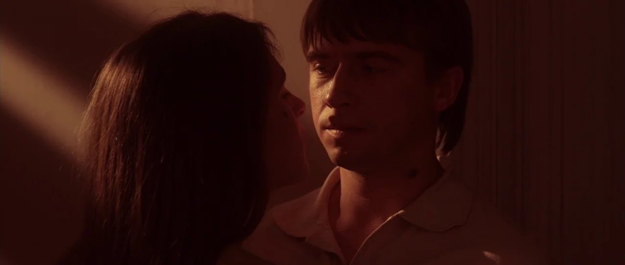 Vanishing Waves (2012) movie still: medium — A dimly lit interior space with a monochromatic red color cast. A young man with brown hair stands near…