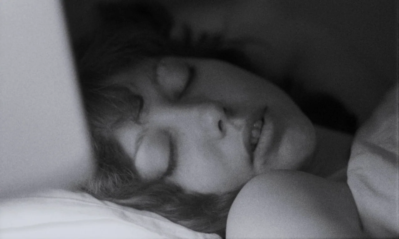 The Secret Son (1979) movie still: closeup — A dark bedroom setting with a person sleeping on a white pillow. The subject lies on their side with…