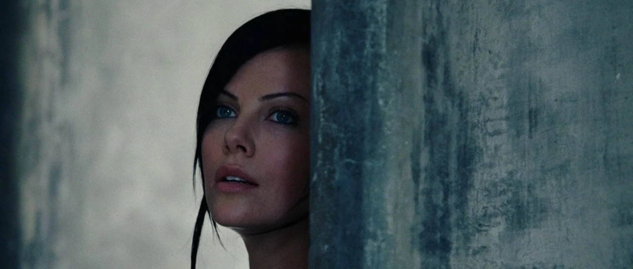 Aeon Flux (2005) movie still: closeup — An interior space features a textured grey concrete wall partially obscuring the view. A woman with dark…