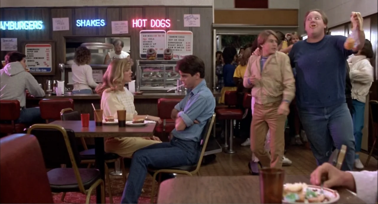 Teen Wolf (1985) movie still: medium — A retro fast food restaurant interior features wood-paneled walls and a busy service counter. A group of…