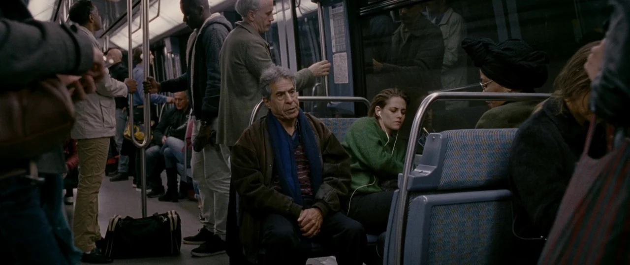 Personal Shopper (2016) movie still: medium — The interior of a modern metropolitan subway car features blue patterned fabric seating. An older man…
