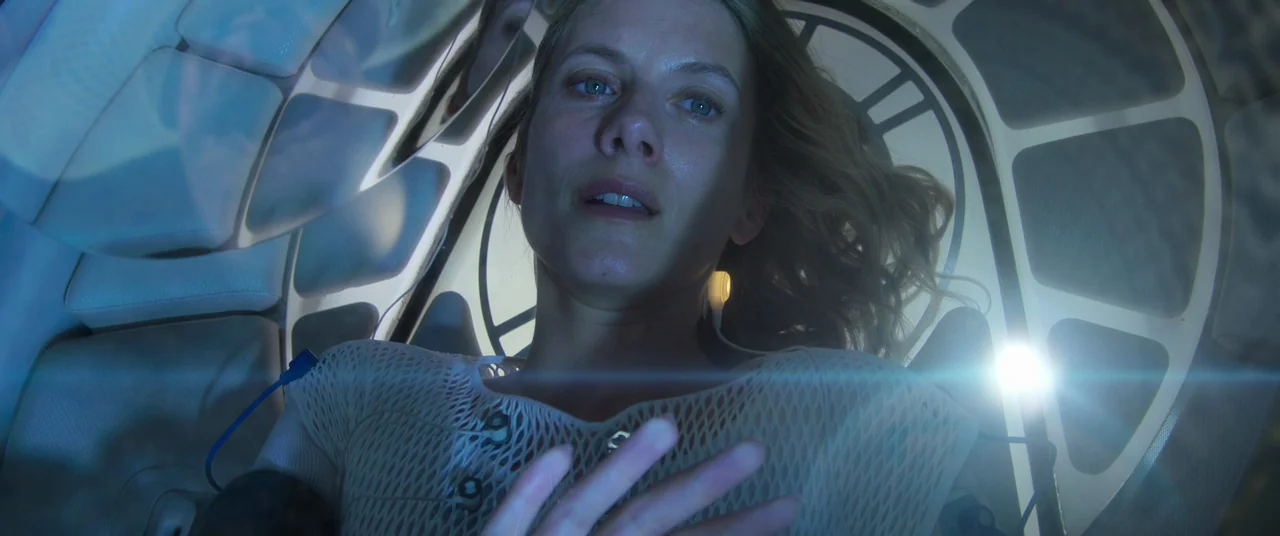 Oxygen (2021) movie still: closeup — A woman lies inside a futuristic medical capsule with internal grid-like structural support patterns. She looks…