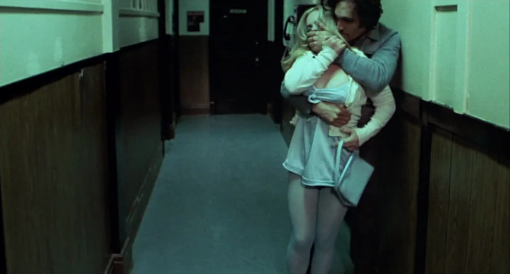 Buffalo ’66 (1998) movie still: fullbody — A narrow apartment corridor with dark wooden wainscoting and stark, light-colored upper walls. A man…