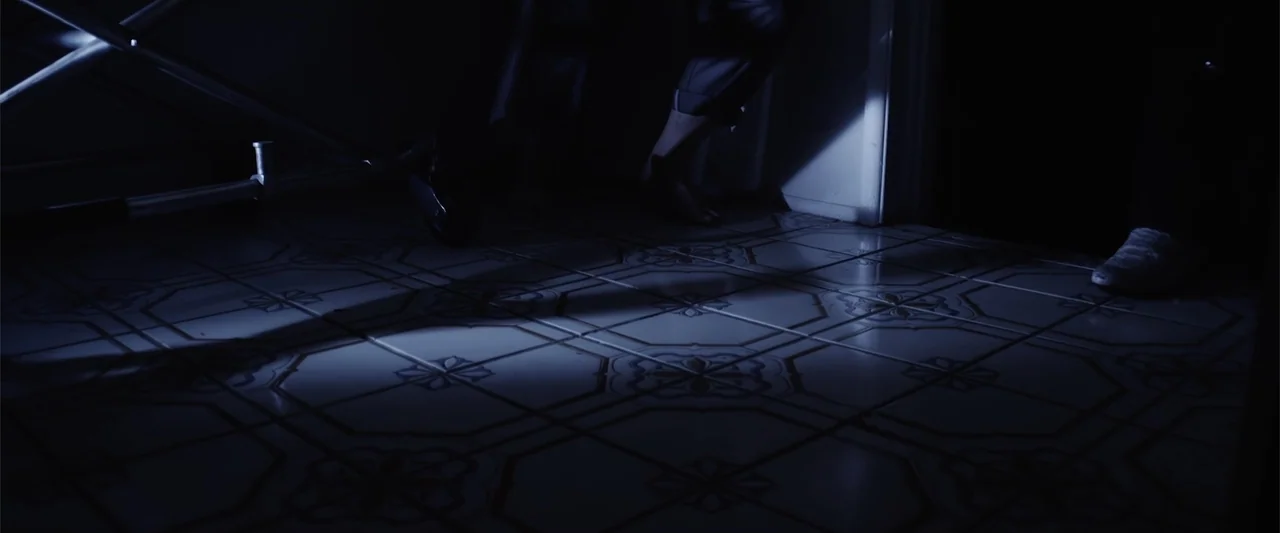 Mermaid Down (2019) movie still: wide — A tiled hallway floor is partially illuminated by a cold light source from above. The rest of the scene…