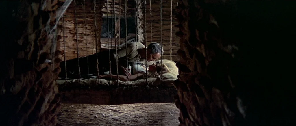 Once Upon A Time In The West (1968) movie still: wide — A dark stone cell with a hanging cot suspended by ropes. A man and a woman lie together on…