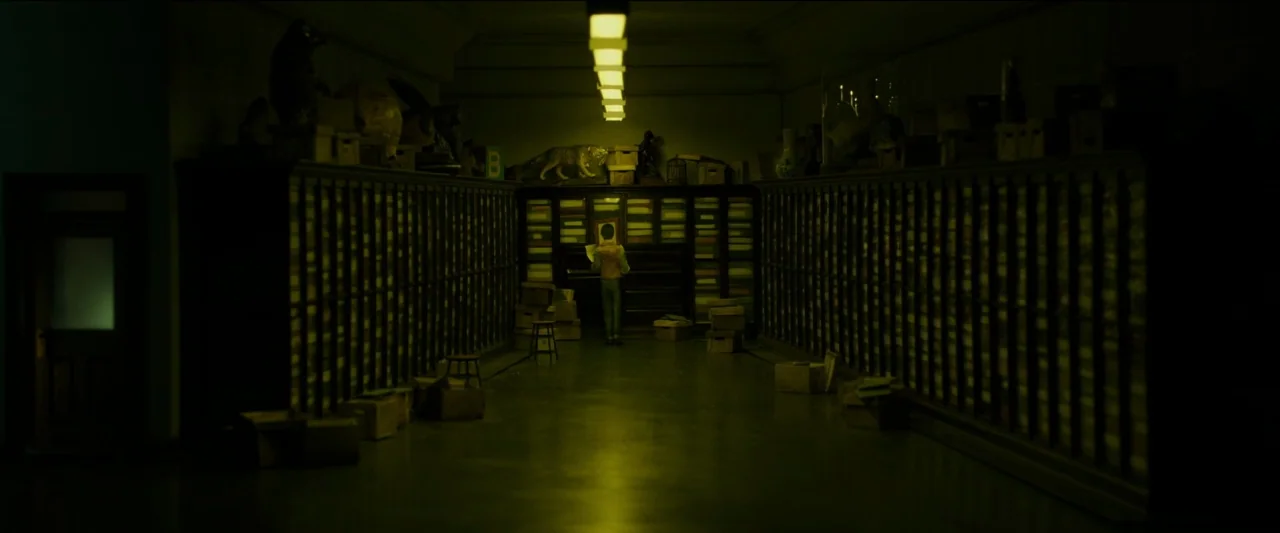 Wonderstruck (2017) movie still: wide — A long, dim aisle is flanked by two walls of floor-to-ceiling wooden storage cabinets. A solitary figure…