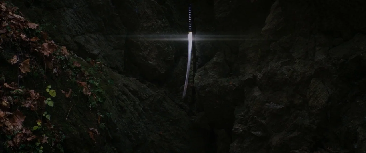 Super Dark Times (2017) movie still: wide — A dark, narrow crevice in a rocky face is covered in damp leaves and moss. A sharp katana blade is…