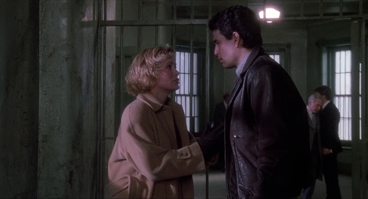 Child’s Play (1988) movie still: medium — A stark room with iron bars separating the foreground and background areas. A man and woman stand facing…