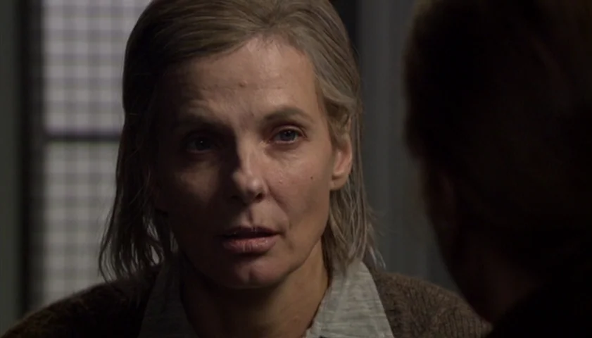 Saraband (2003) movie still: closeup — A woman stands in a dimly lit room with a metallic grate in the background. She faces forward while speaking…