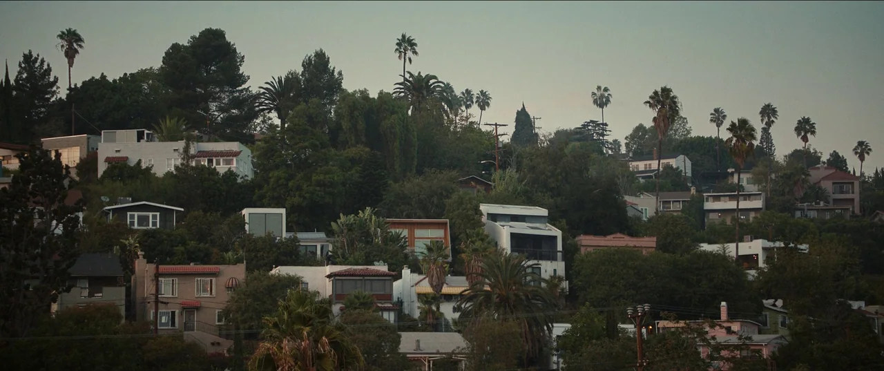 The Greatest Hits (2024) movie still: establishing — A dense collection of houses is built onto a steep, tree-covered suburban hillside. The…