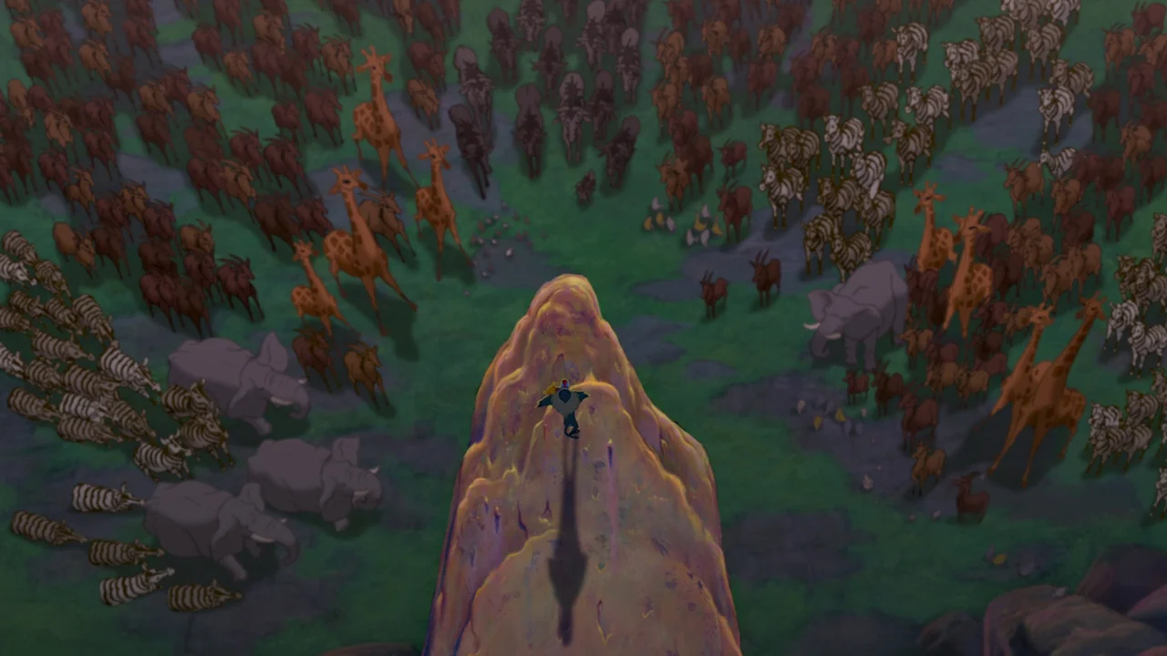 The Lion King (1994) movie still: wide — A high-angle view shows a large herd of animals surrounding a tall cliff peak. A solitary dark figure…