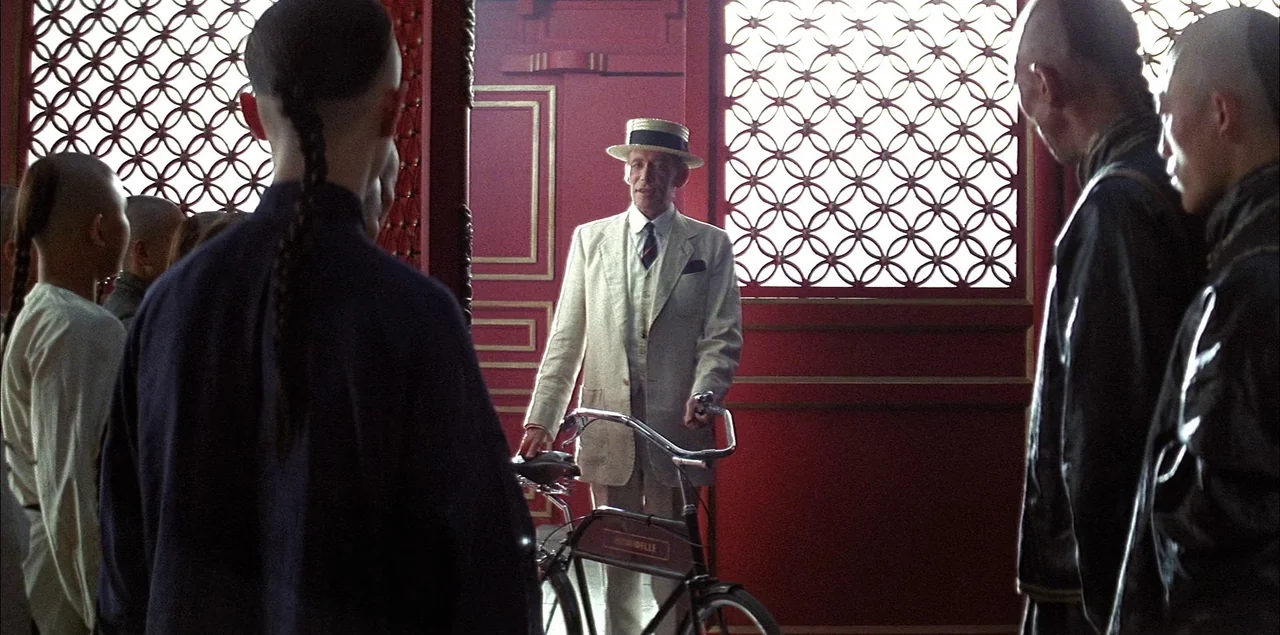 The Last Emperor (1987) movie still: medium — A long hallway within a palace features walls of deep red and lattice woodwork. A European man in a…