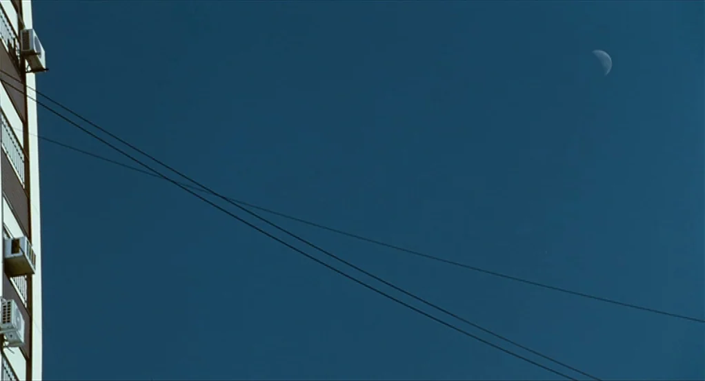 Sidewalls (2011) movie still: establishing — A tall apartment building facade with air conditioning units protrudes from the left edge. A crescent…