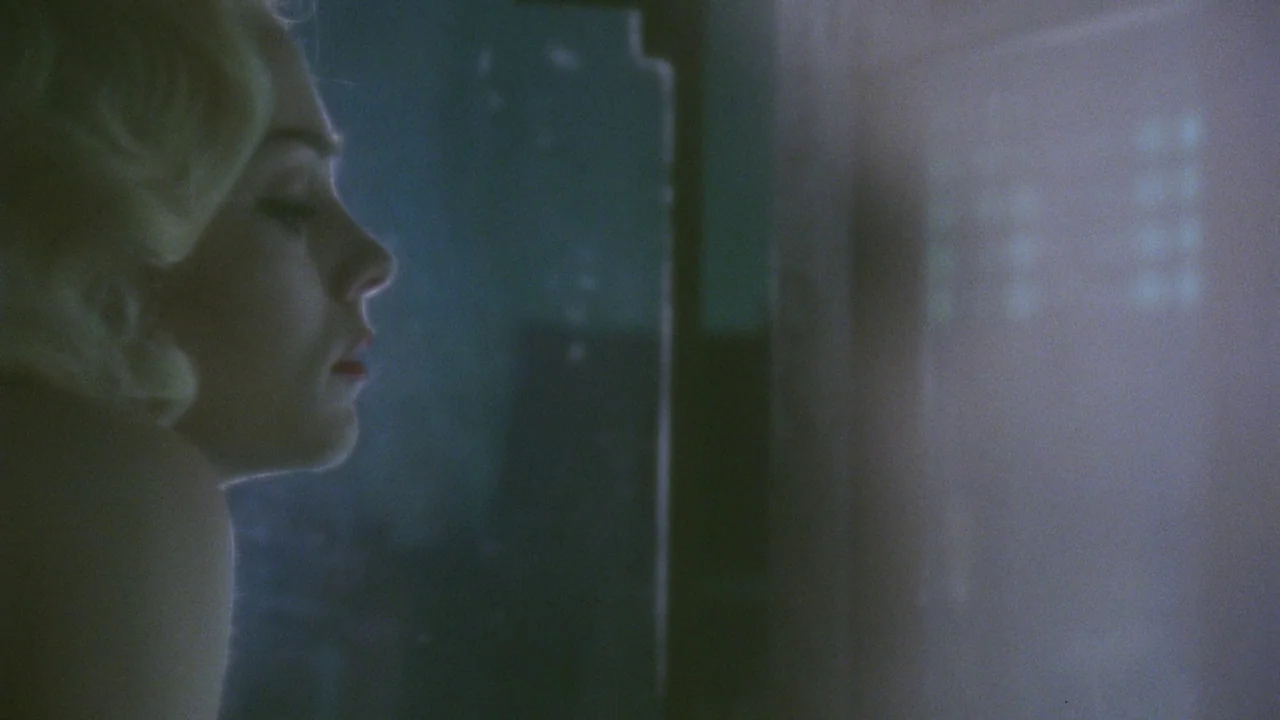 Insignificance (1985) movie still: closeup — A dark, cramped tiled space features a single person positioned behind a glass panel. A woman with…