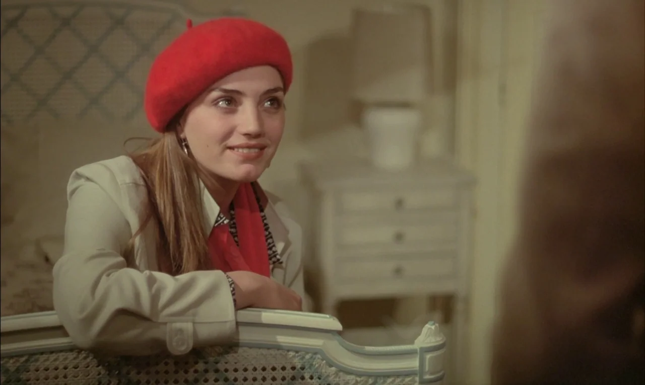 That Obscure Object of Desire (1977) movie still: medium — A woman leans over the end of a white wooden bed frame. She wears a vibrant red beret and…