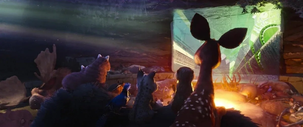 The Wild Robot (2024) movie still: wide — Various woodland animals sit together inside a cavern looking at a projected movie screen. The screen…