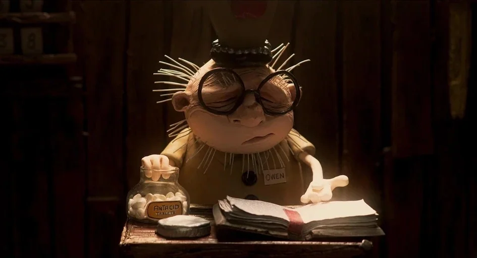 Memoir of a Snail (2024) movie still: medium — A dimly lit room contains a small wooden desk holding a book and medicine. A stop-motion character…