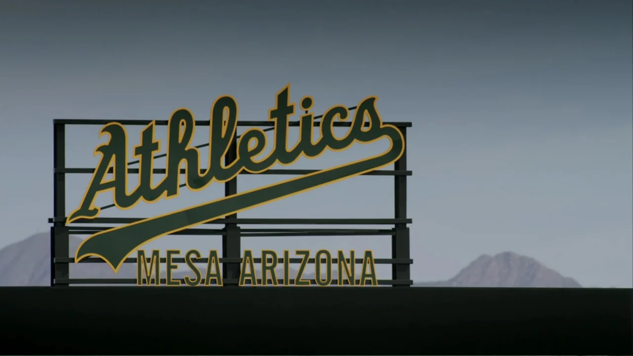 Ferrell Takes the Field (2015) movie still: wide — A metal sign with green and gold lettering sits against a clear blue sky. Distant mountains are…
