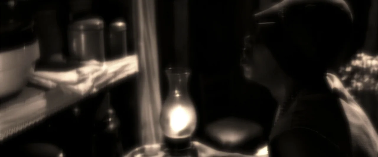 A Family Thing (1996) movie still: closeup — A dark interior room contains a shelf with canisters and a small oil lamp. A person sits in the…