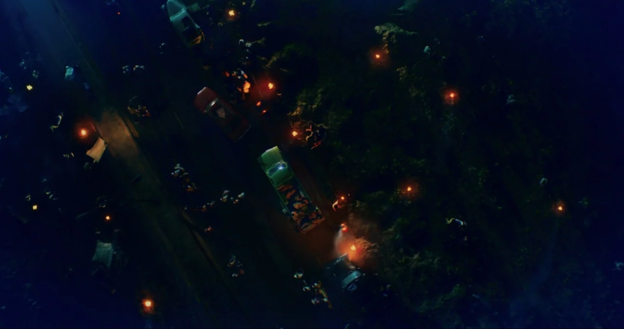 First They Killed My Father (2017) movie still: establishing — A dark road at night is occupied by several vehicles and clusters of people. Small…